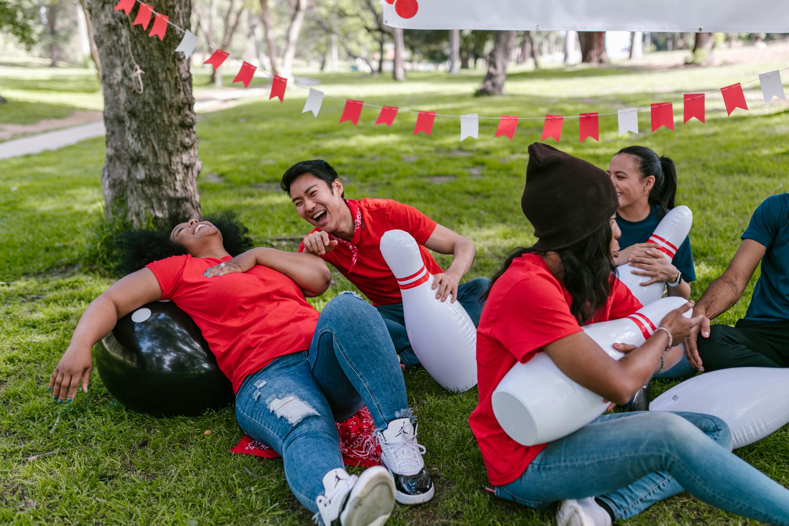 Diverse friends having fun with inflatable bowling pins in a park on a sunny day.